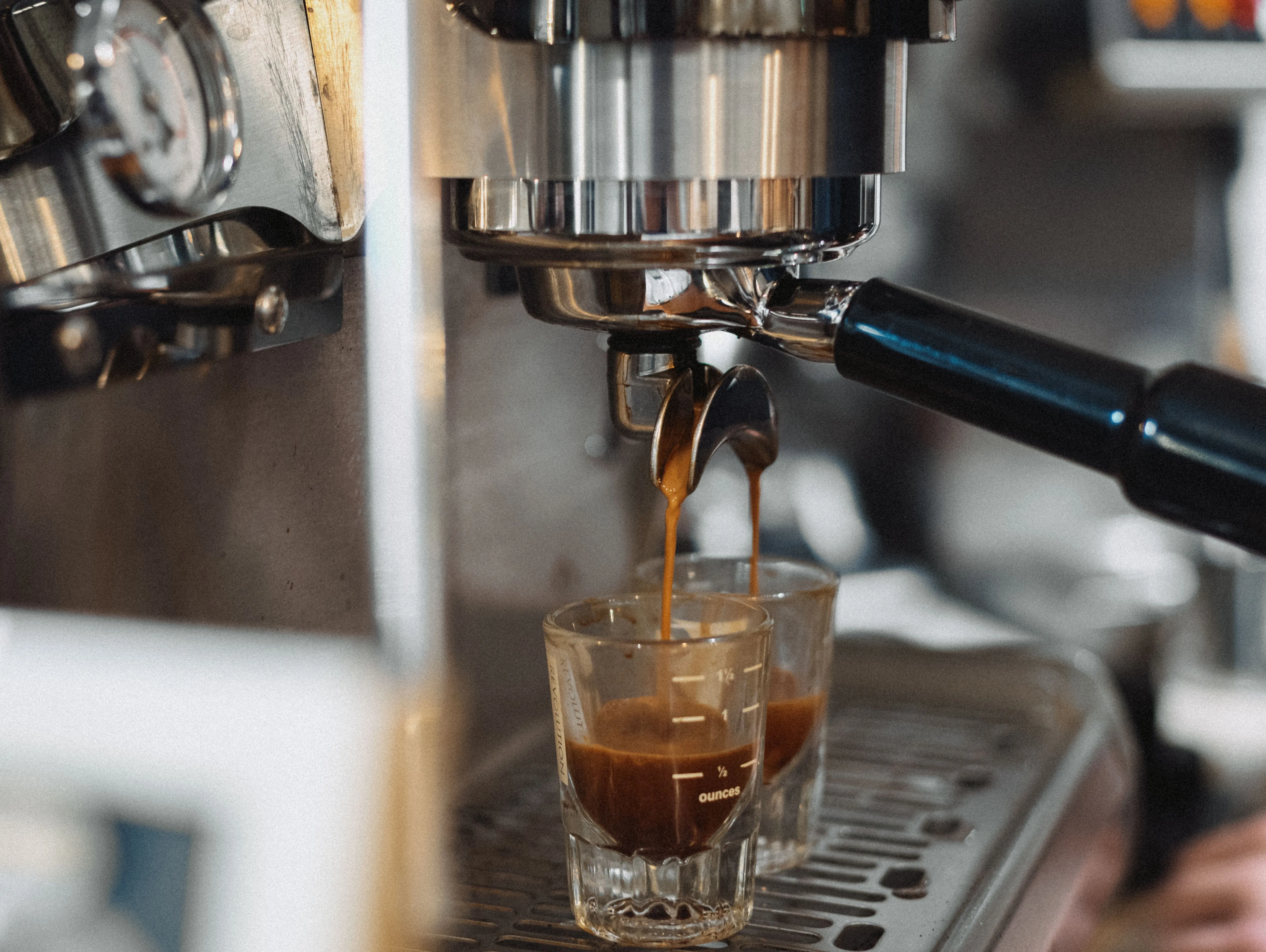 Espresso pouring from portafilter into two shot glasses on machine