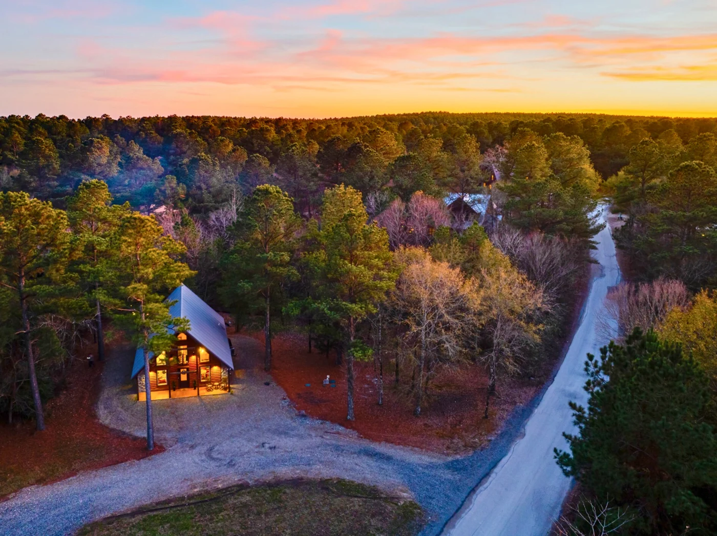 An evening aerial of Hearth and Heritage glowing beneath the trees beside its cabin-community road