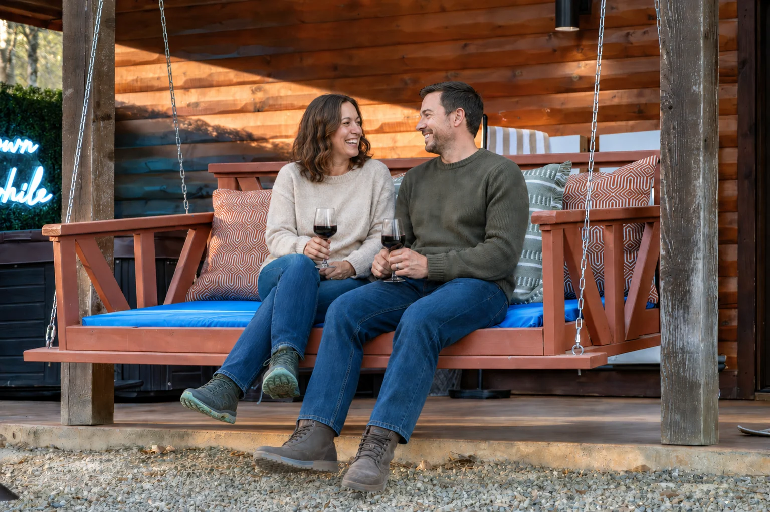A couple holding wine glasses on the daybed swing at Hearth and Heritage