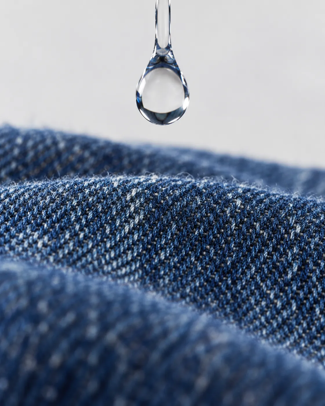 A clear water drop suspended just above raw indigo denim.