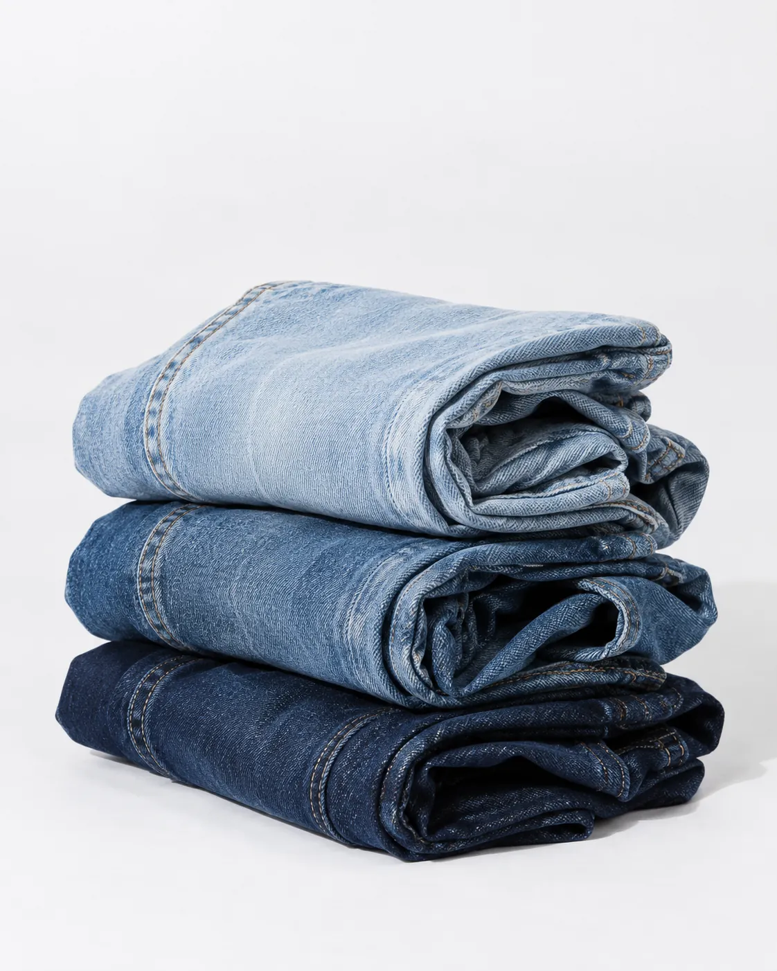 Three folded pairs of jeans in dark, mid and pale blue washes.