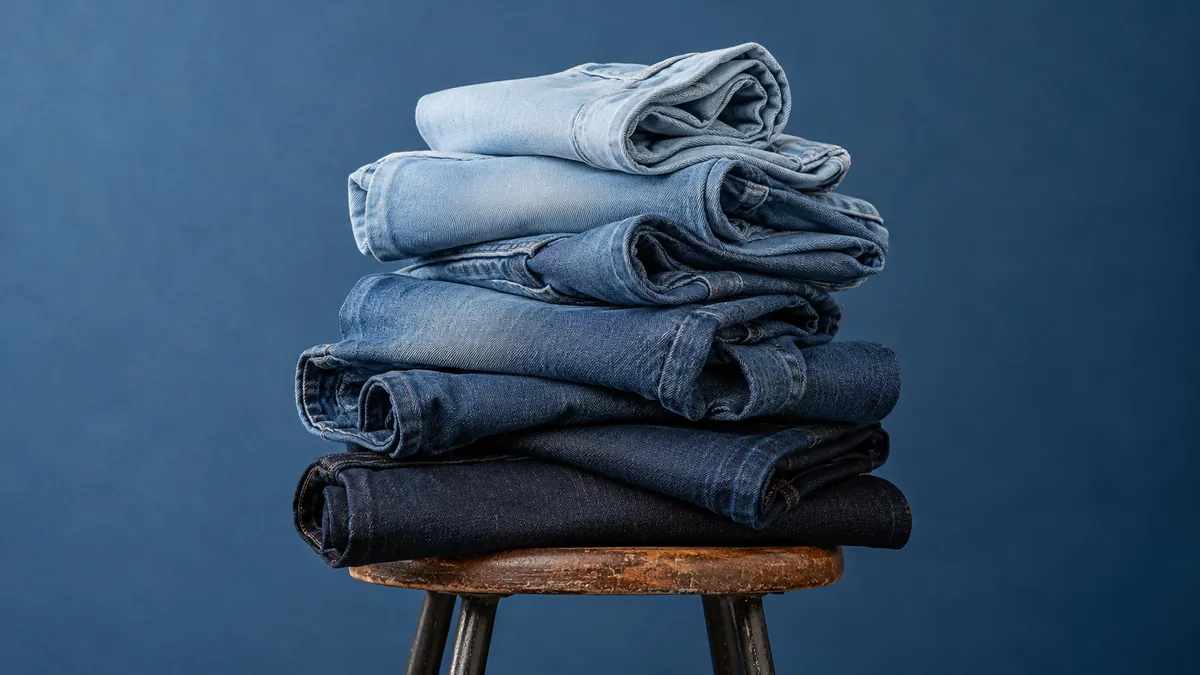 A stack of folded jeans ranging from raw indigo to bleached blue on a stool.