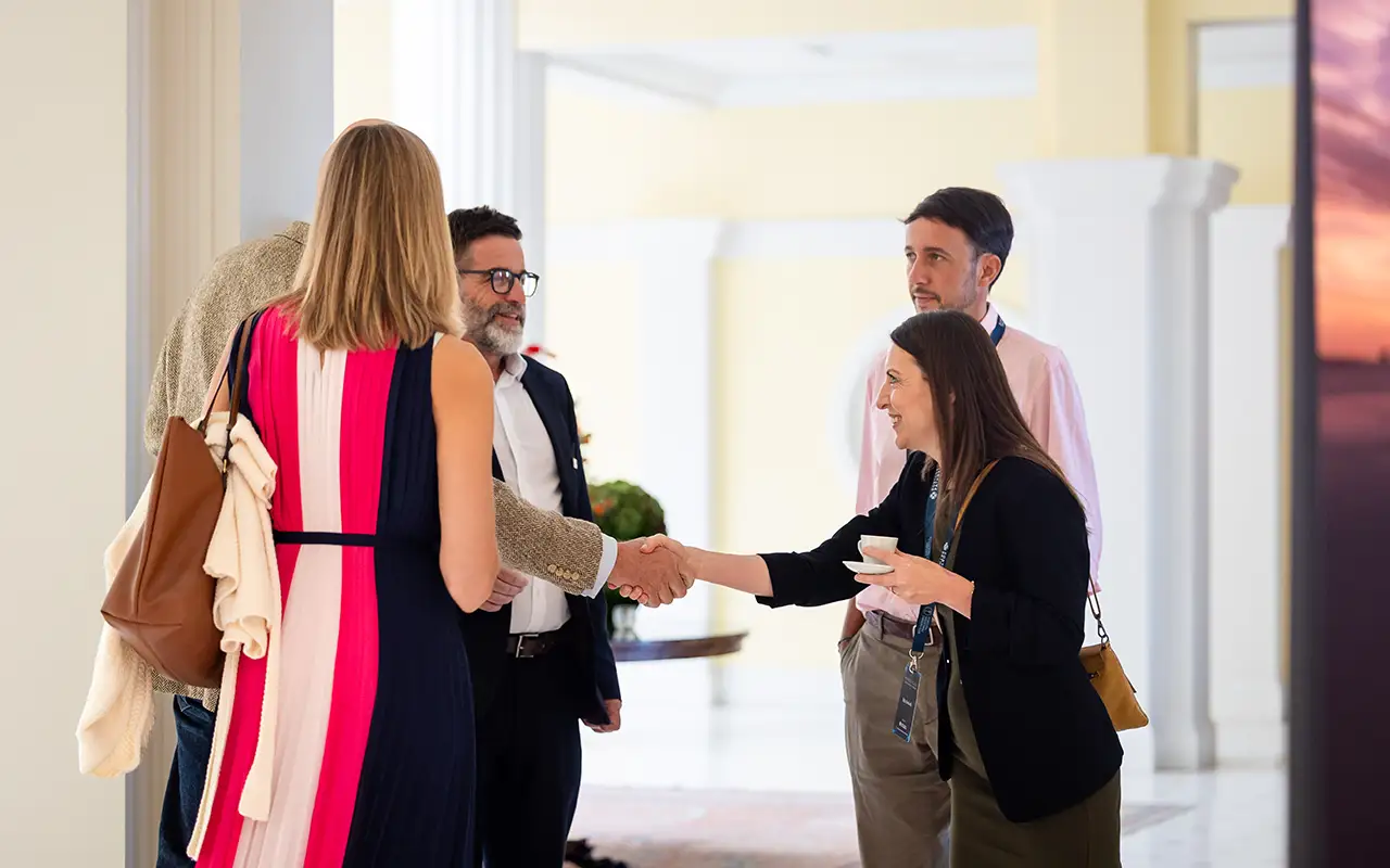 Delegates exchange a handshake while others look on in the hallway