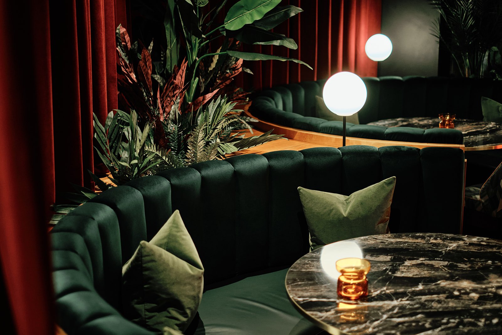 Green velvet curved booth with globe lamps and red curtains at The Porter's Store, St Helier, Jersey