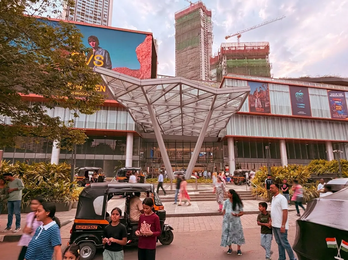 Crowds and auto-rickshaws outside the SkyCity Mall entrance canopy by day, Mumbai