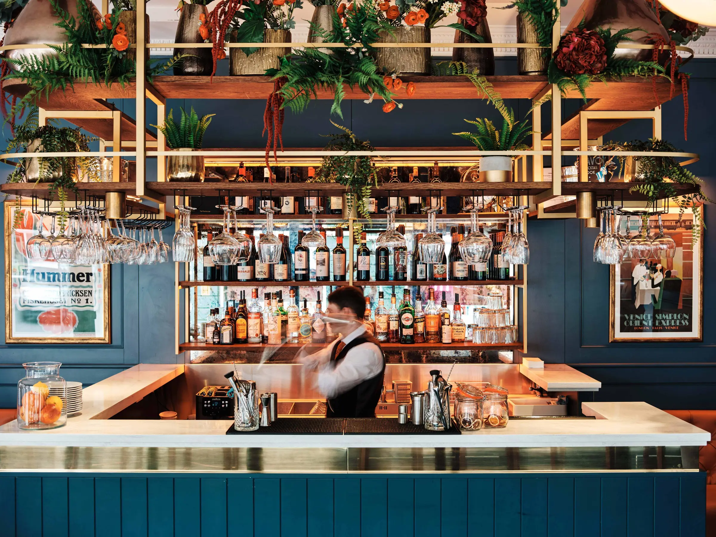 Brass bar with hanging plants and back-lit bottles at The Watchmaker wine bar, St Helier, Jersey
