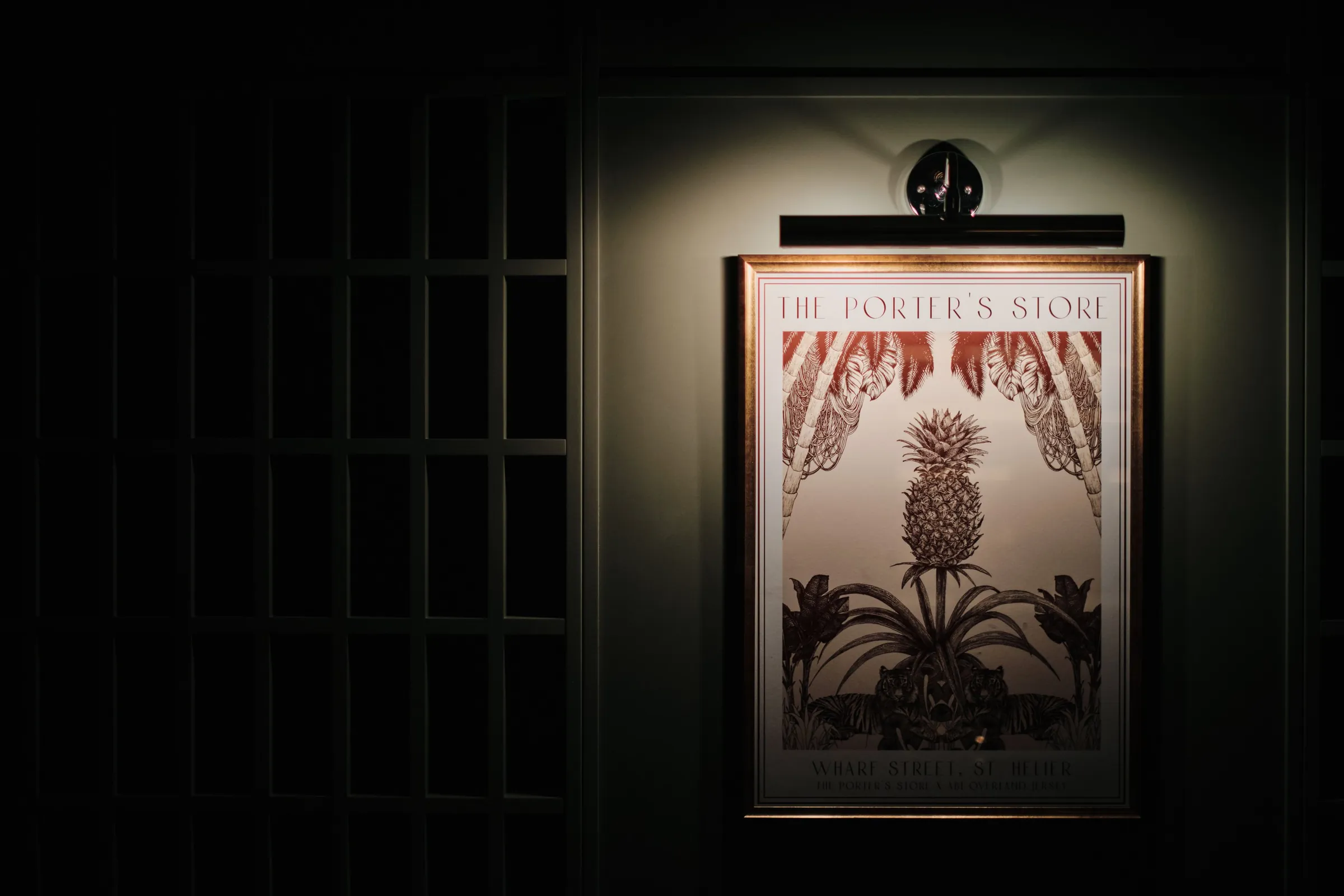 Framed pineapple print reading 'The Porter's Store' on a dark green wall