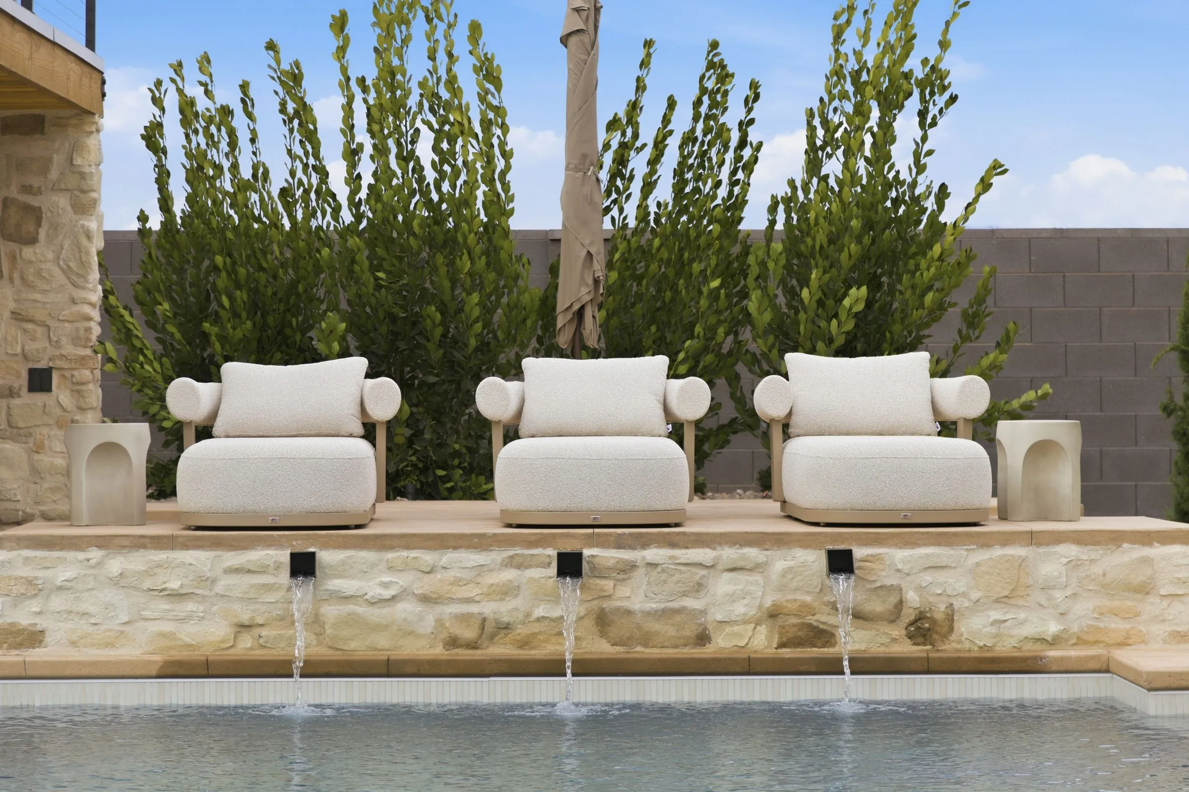 Three lounge chairs above a pool with waterfall spouts