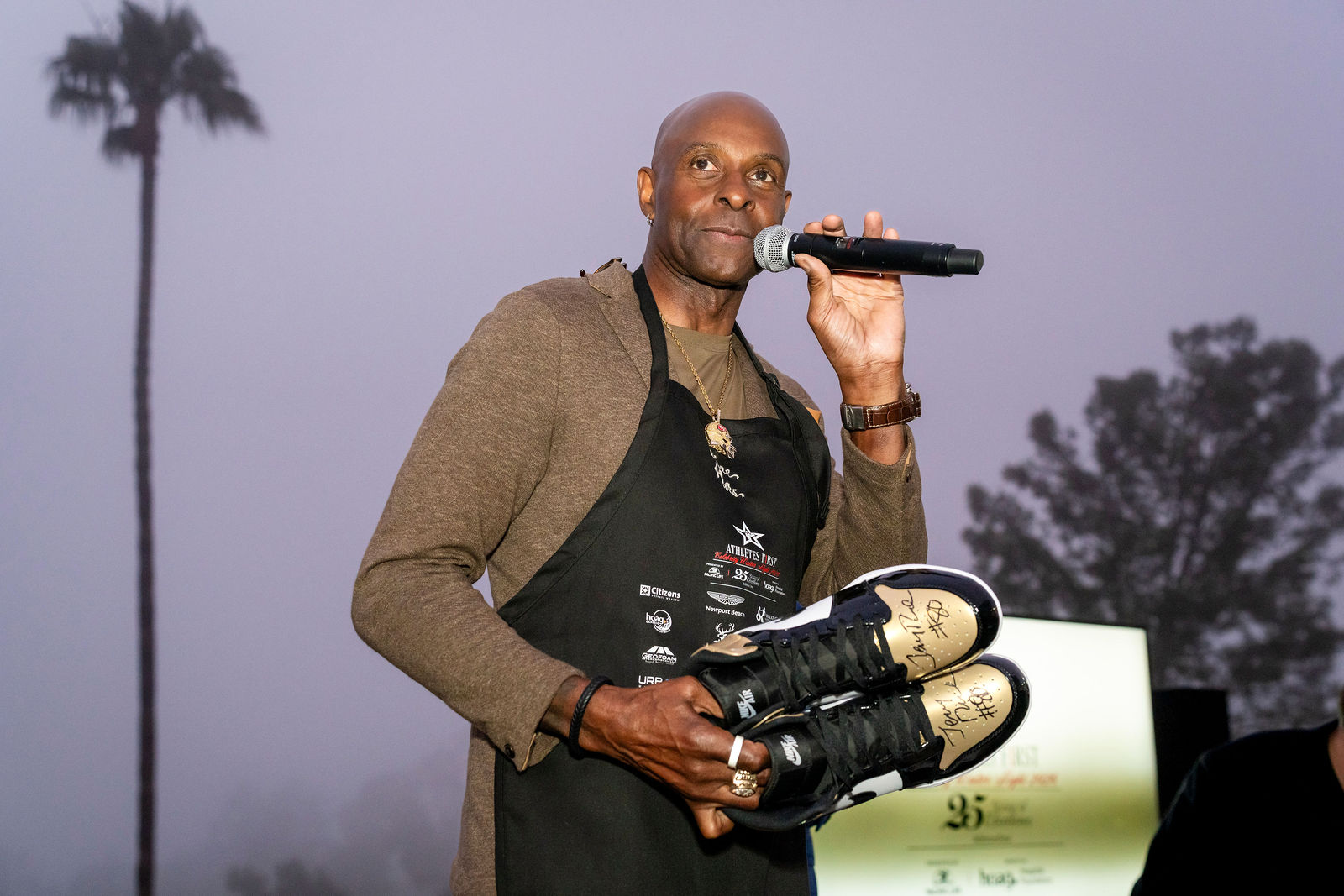 Jerry Rice at the microphone holding autographed shoes for the auction