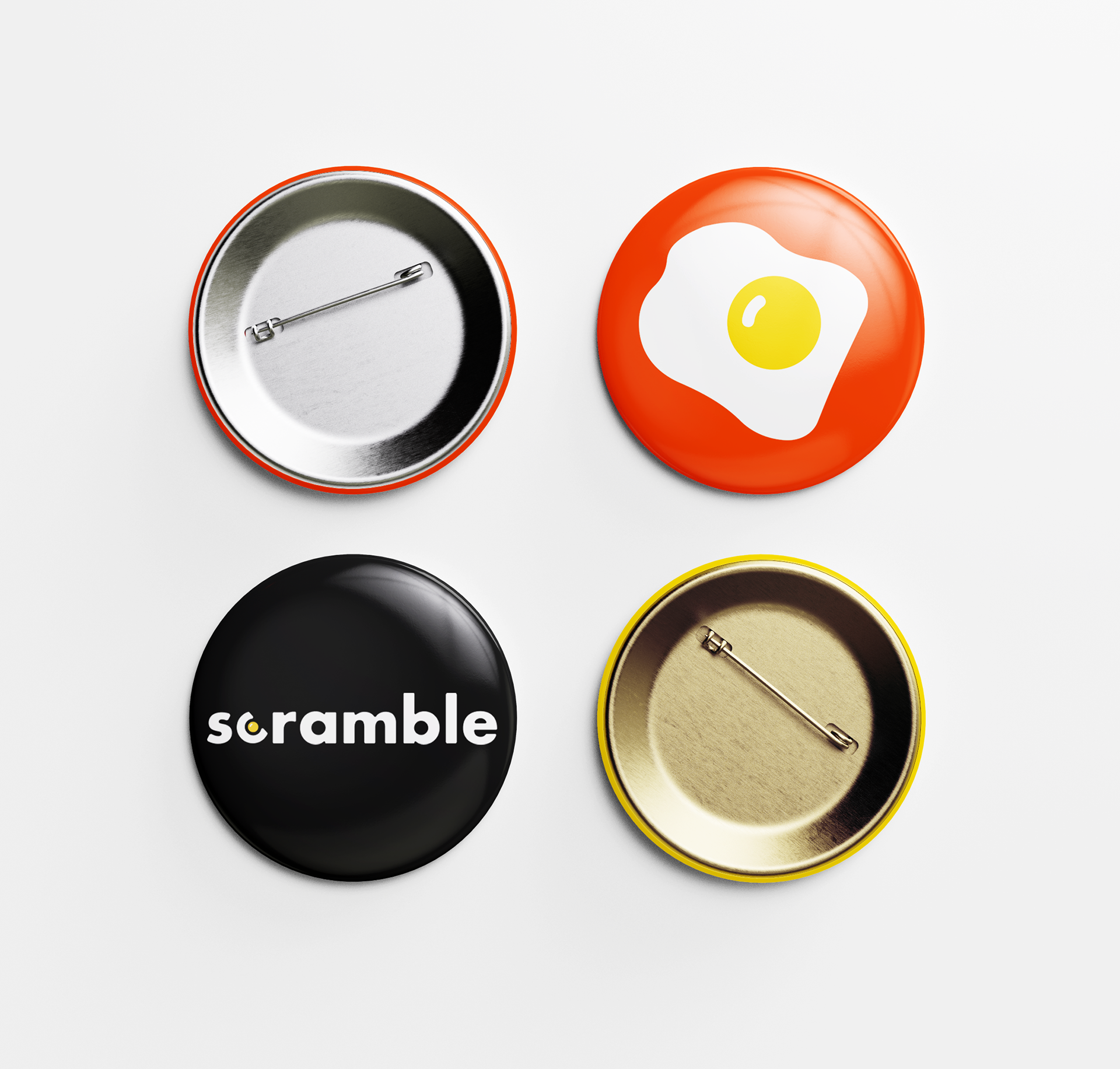 Four round Scramble pin buttons: an orange egg design, a black one with the white scramble wordmark, and two showing the metal backs with pins.