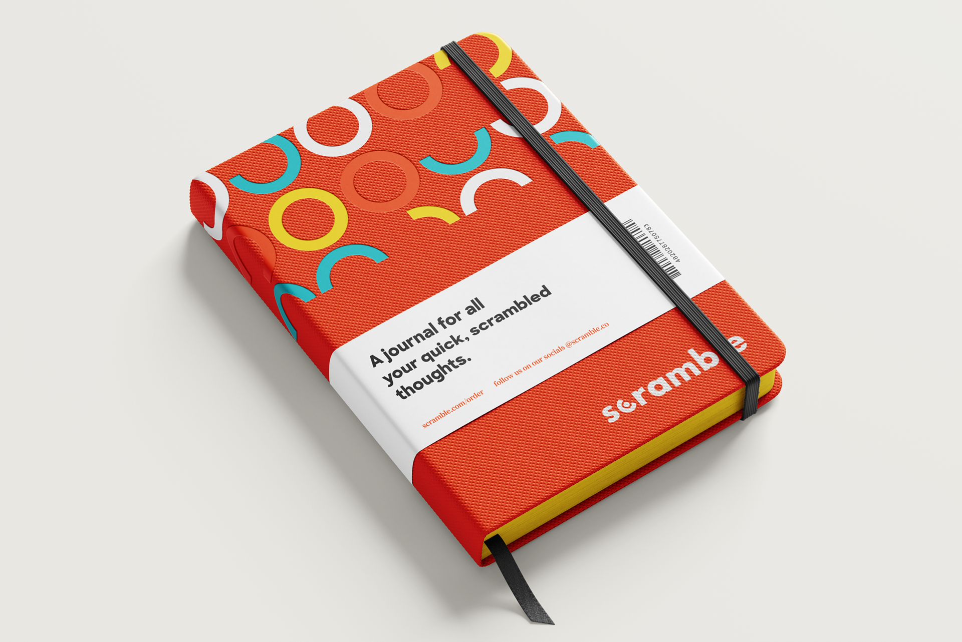 Scramble hardcover notebook in orange with the ring pattern, a black elastic band and a white wrap reading "A journal for all your quick, scrambled thoughts."