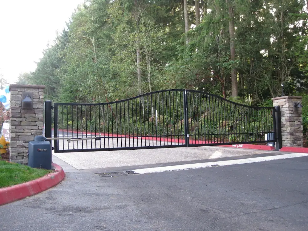 Black swing gate with operator arm and stone pillars at a community entrance