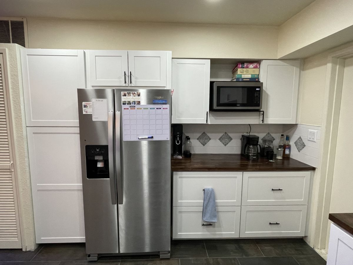 The same kitchen after the remodel, with white cabinets, butcher-block counters and a stainless refrigerator