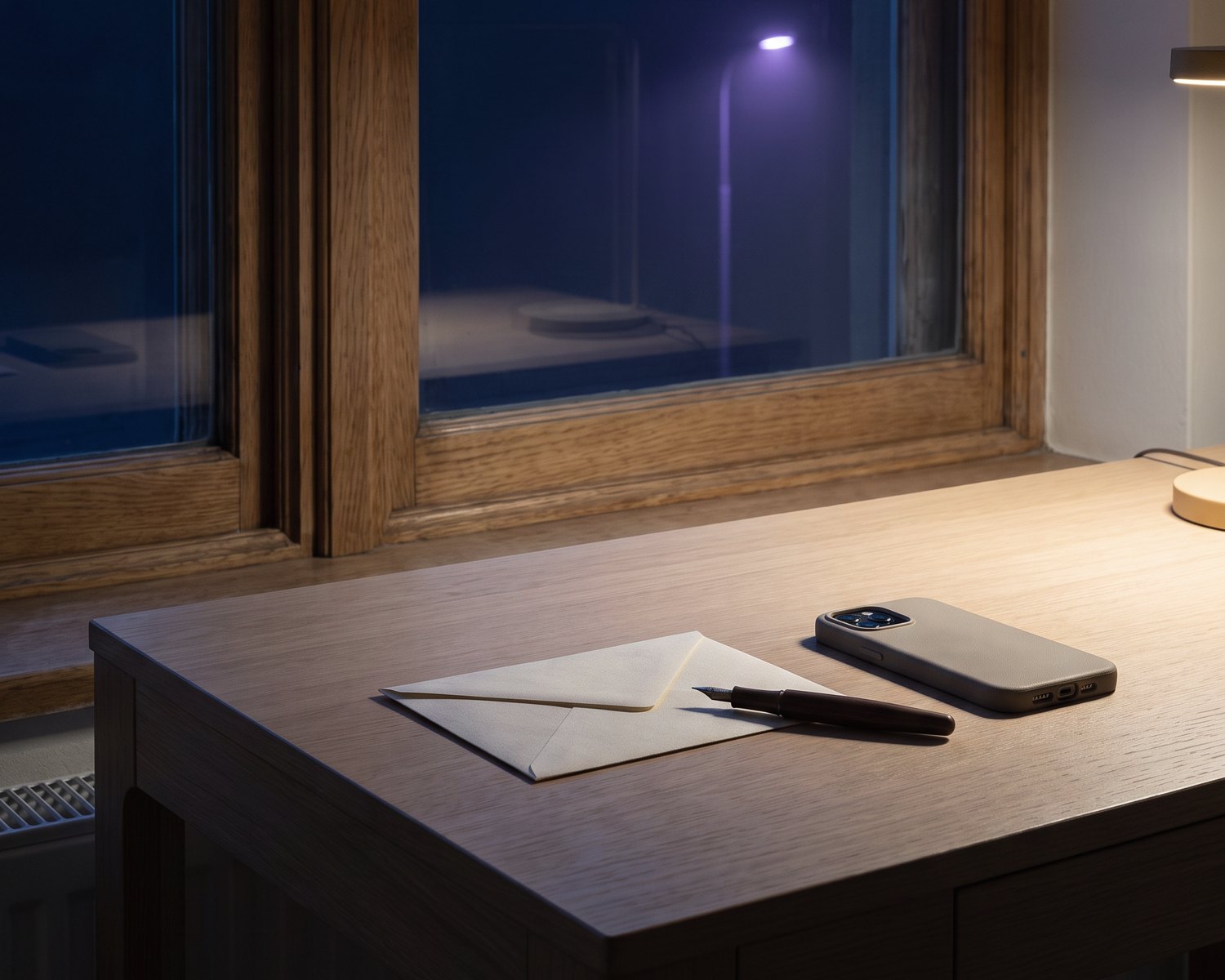 A tidy oak desk by a window at blue hour with one envelope, a fountain pen and a phone.