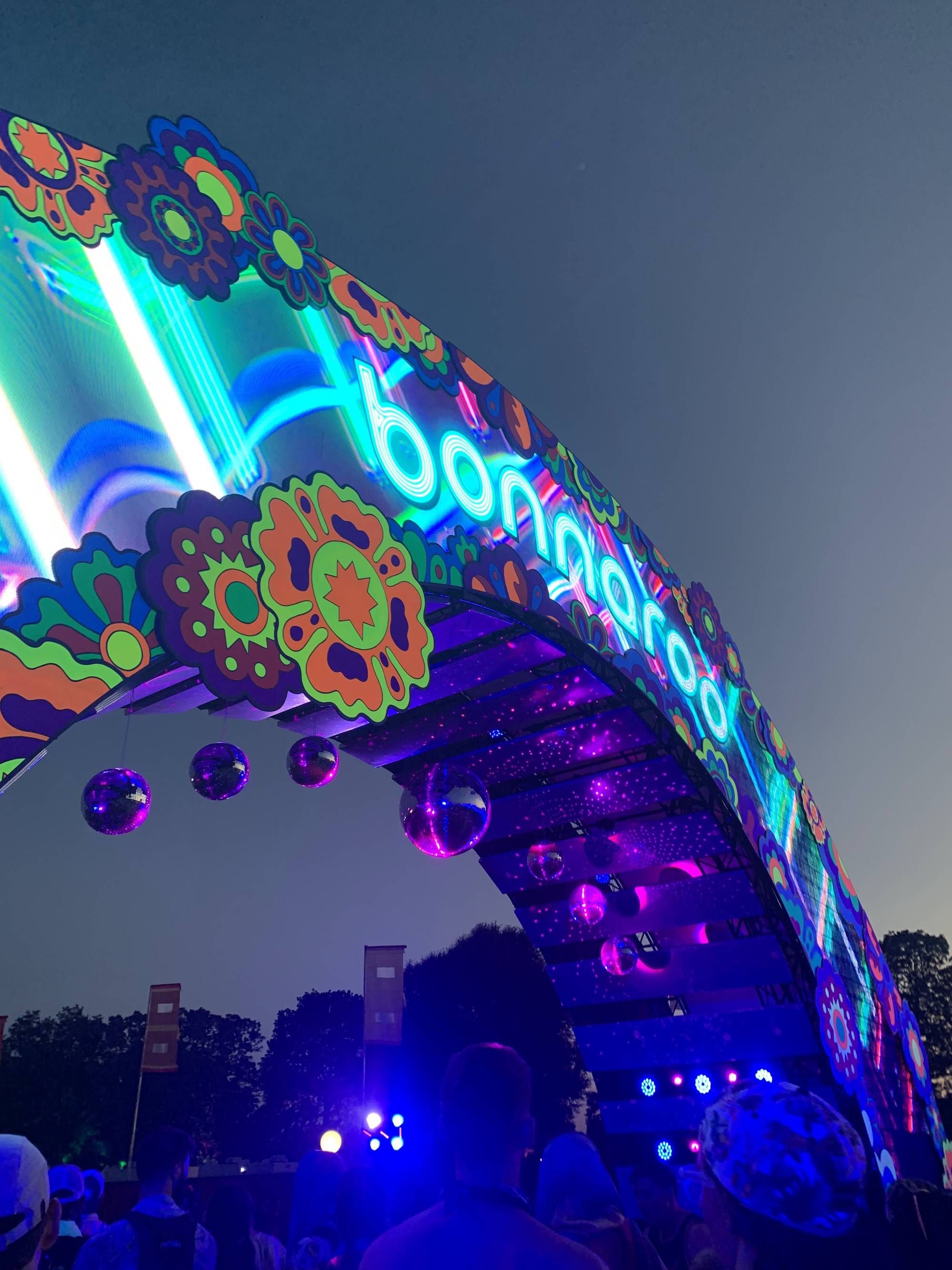 Colorful flower-covered Bonnaroo arch with the glowing 'bonnaroo' sign and mirror balls at dusk, Bonnaroo Music and Arts Festival, Manchester, Tennessee