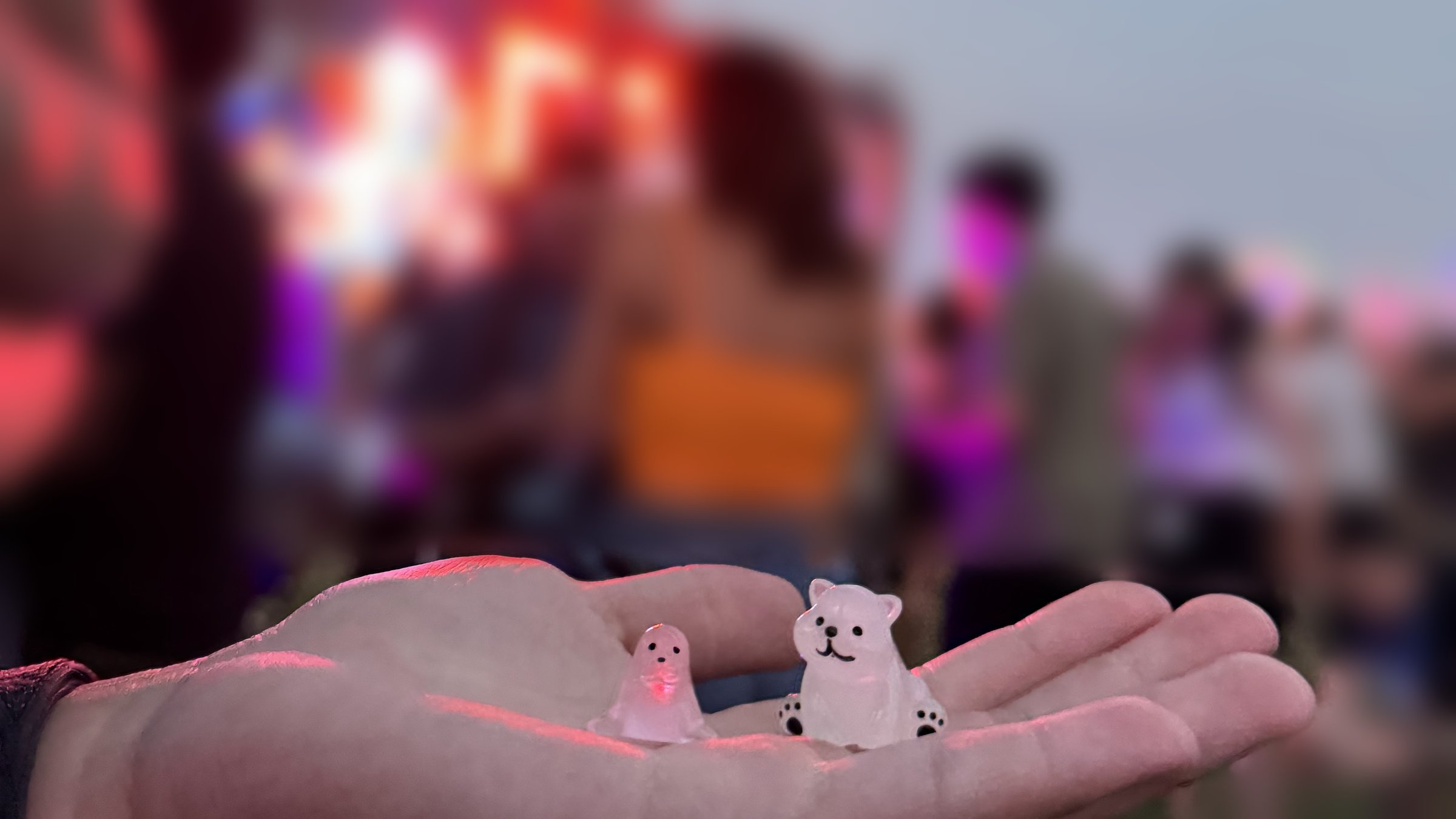 Two small glass animal trinkets held in a palm at a festival at dusk