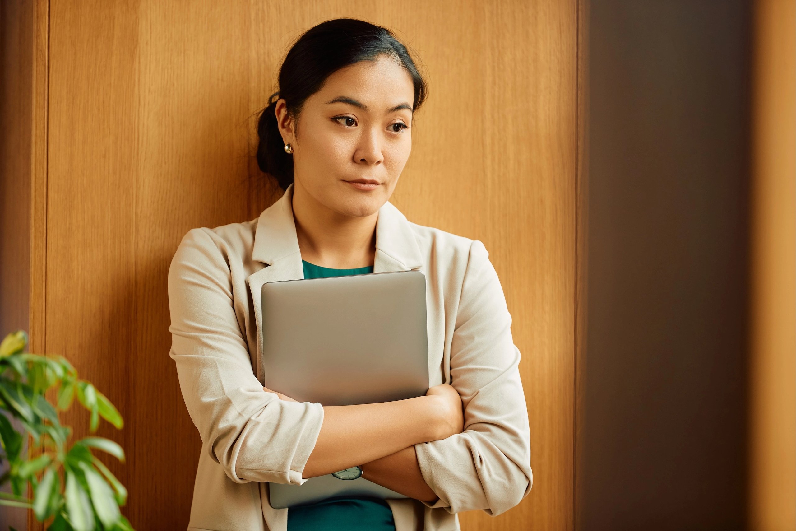 Woman holding a laptop, looking thoughtful in a quiet room