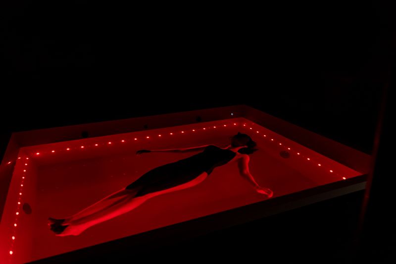 Une personne flotte dans le bassin de la Floatroom de DAO Mons, éclairé de rouge