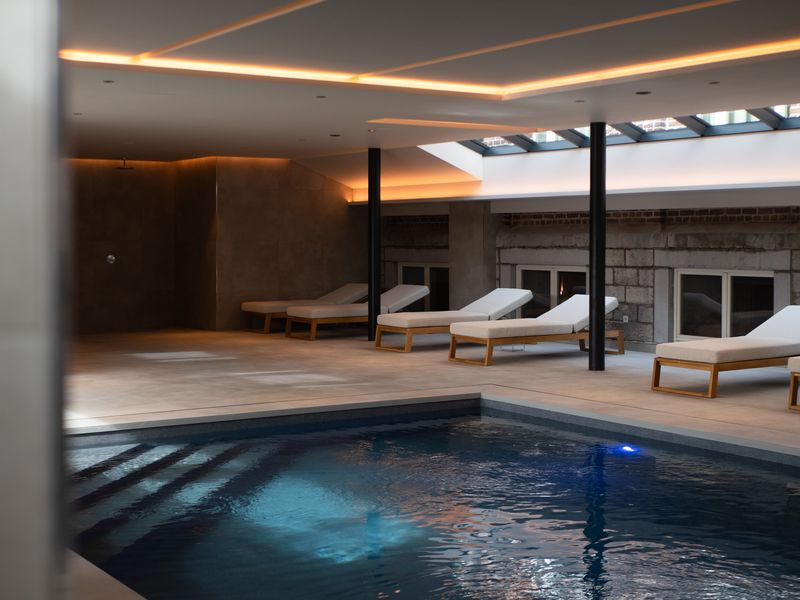 La piscine chauffée de DAO Verviers et ses bains de soleil, sous un plafond aux lignes de lumière