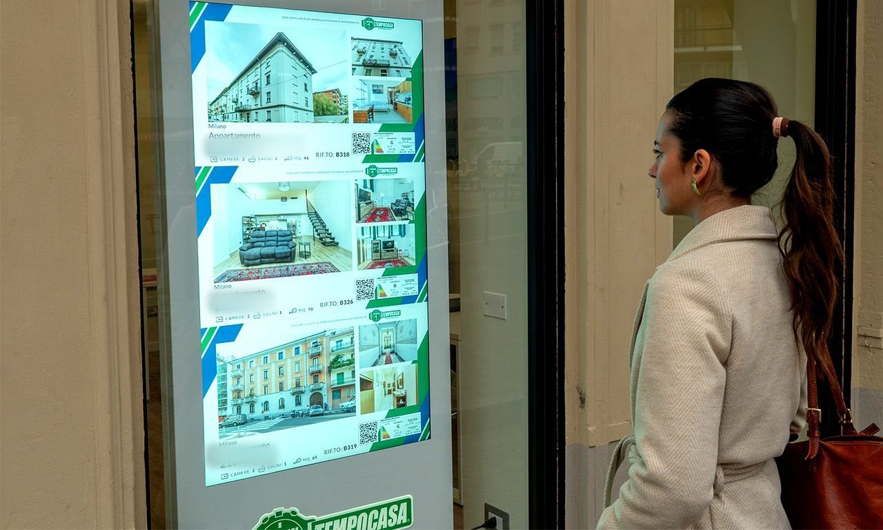 Una passante guarda gli annunci sul totem in vetrina di un'agenzia Tempocasa