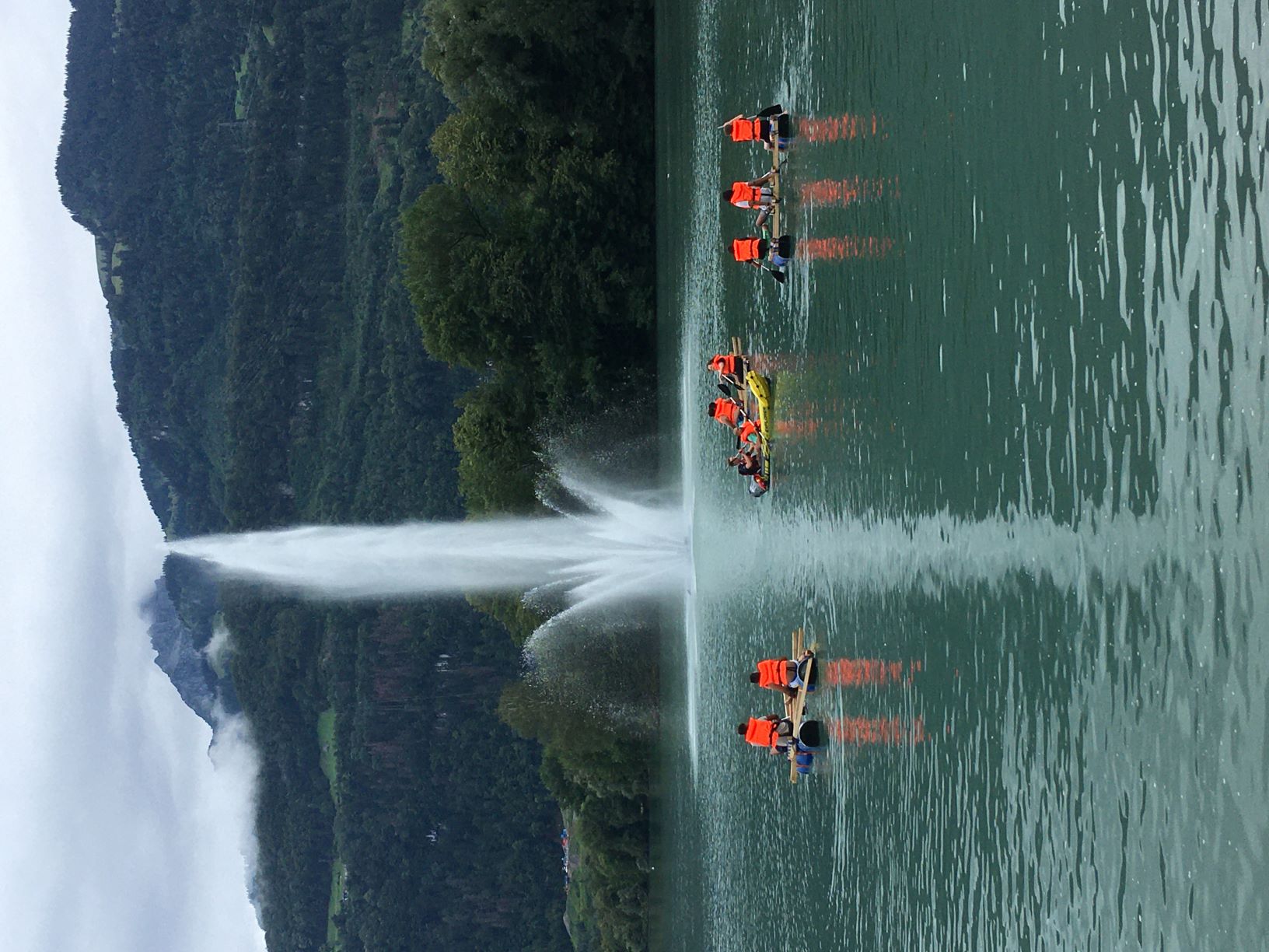 Mehrere selbst gebaute Flosse mit Kindern in orangen Schwimmwesten auf einem See