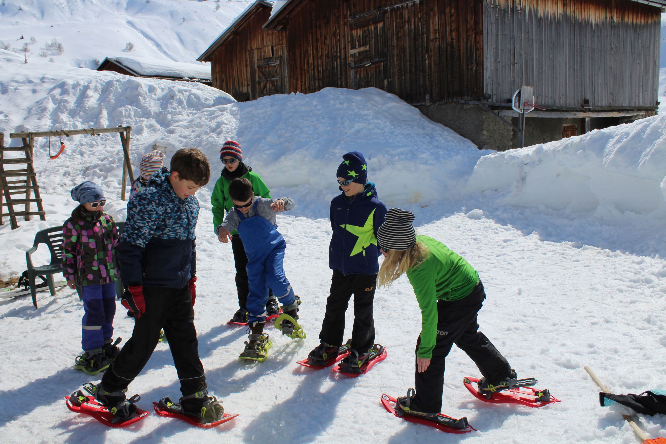 Kinder probieren vor einer Holzscheune ihre Schneeschuhe aus