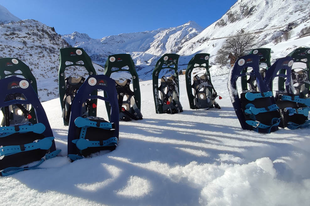 Schneeschuhe stehen aufgereiht im Schnee vor verschneiten Bergen