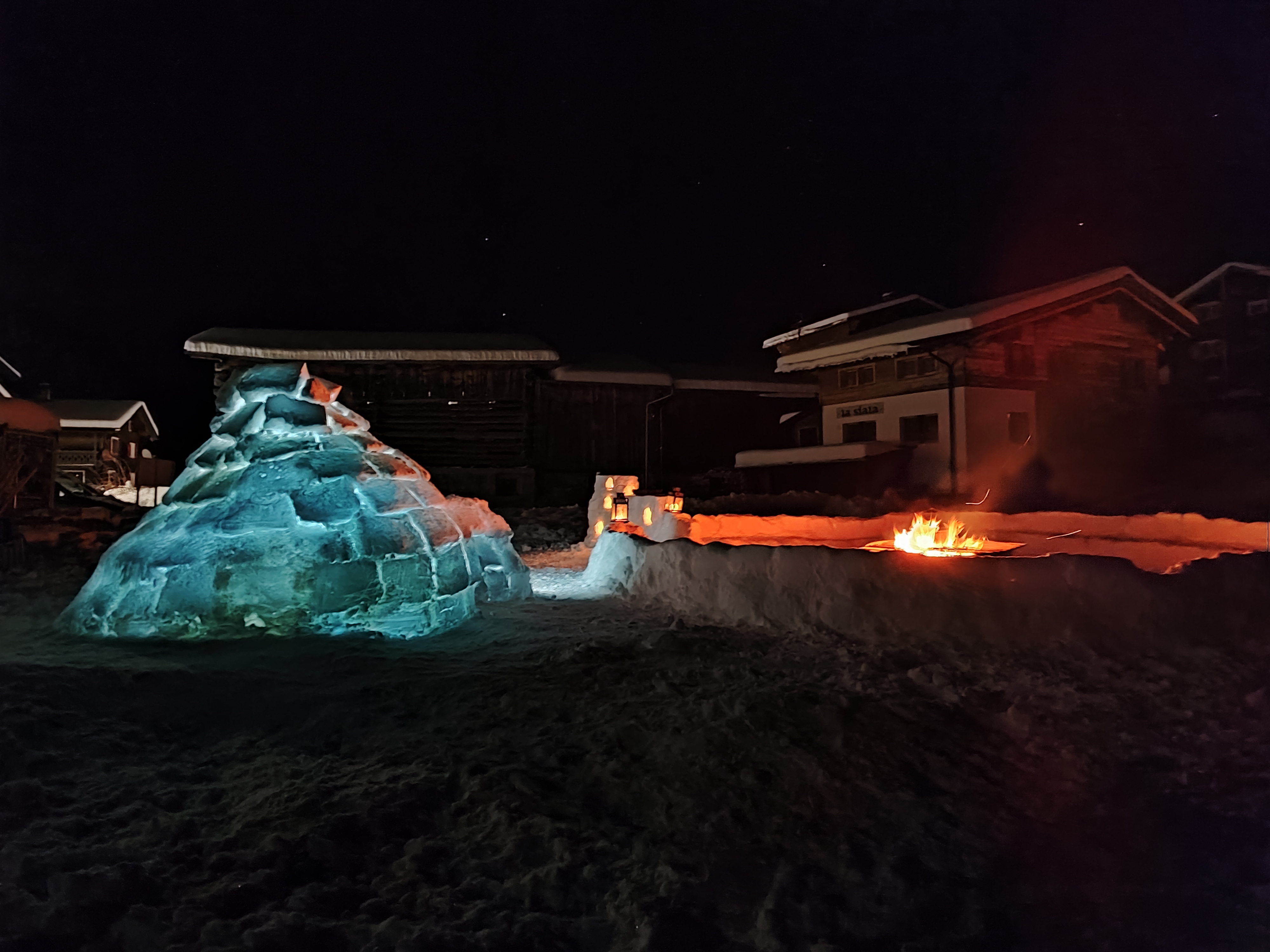 Beleuchtetes Iglu und Feuerstelle im Schnee bei Nacht