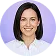 Smiling woman with short dark hair wearing a white collared shirt against a purple background.
