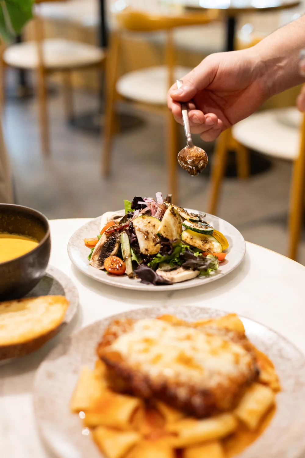 A hand drizzles dressing over a fresh vegetable salad at Amand.
