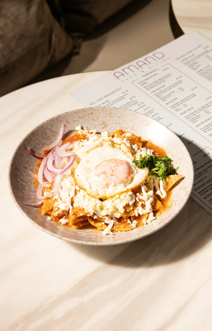 Chilaquiles topped with a fried egg, cheese and onion beside the Amand menu.