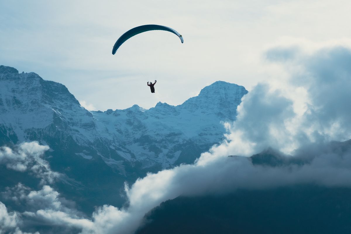 Paraglider flying above dramatic snow-covered mountains