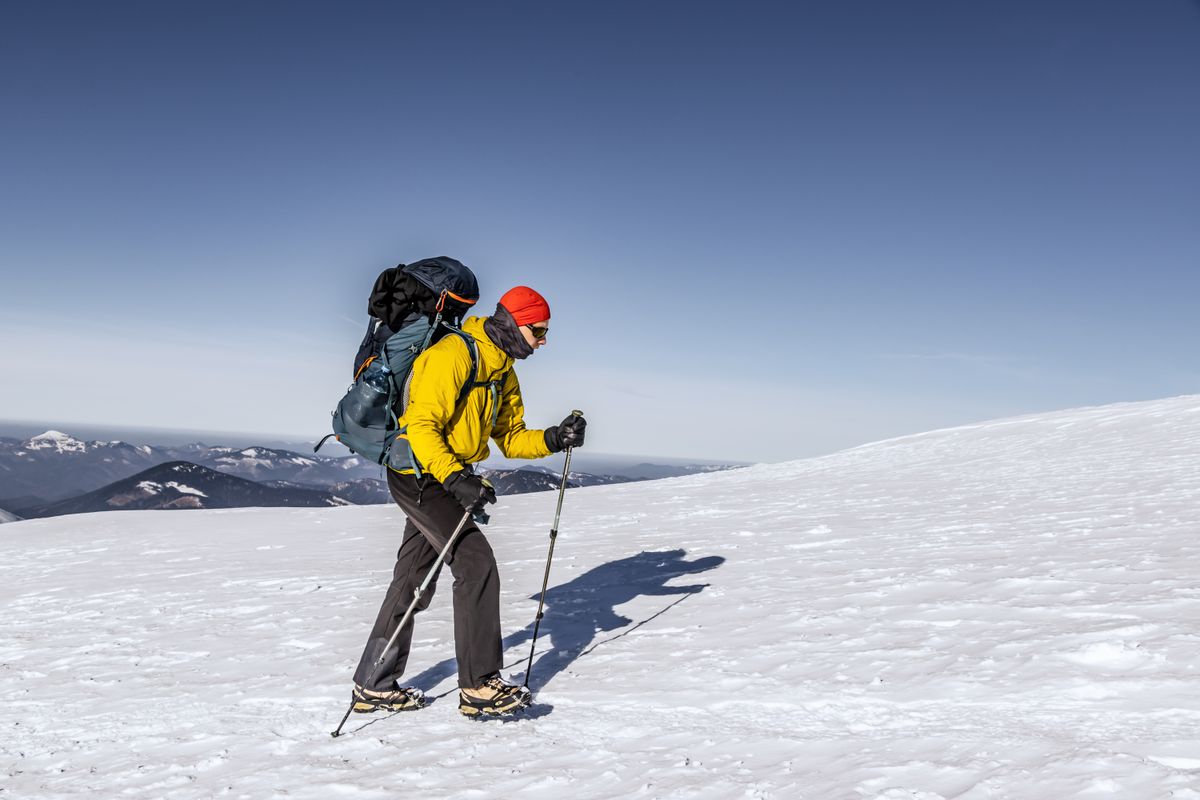 Mountaineer ascending a snow-covered summit with trekking poles