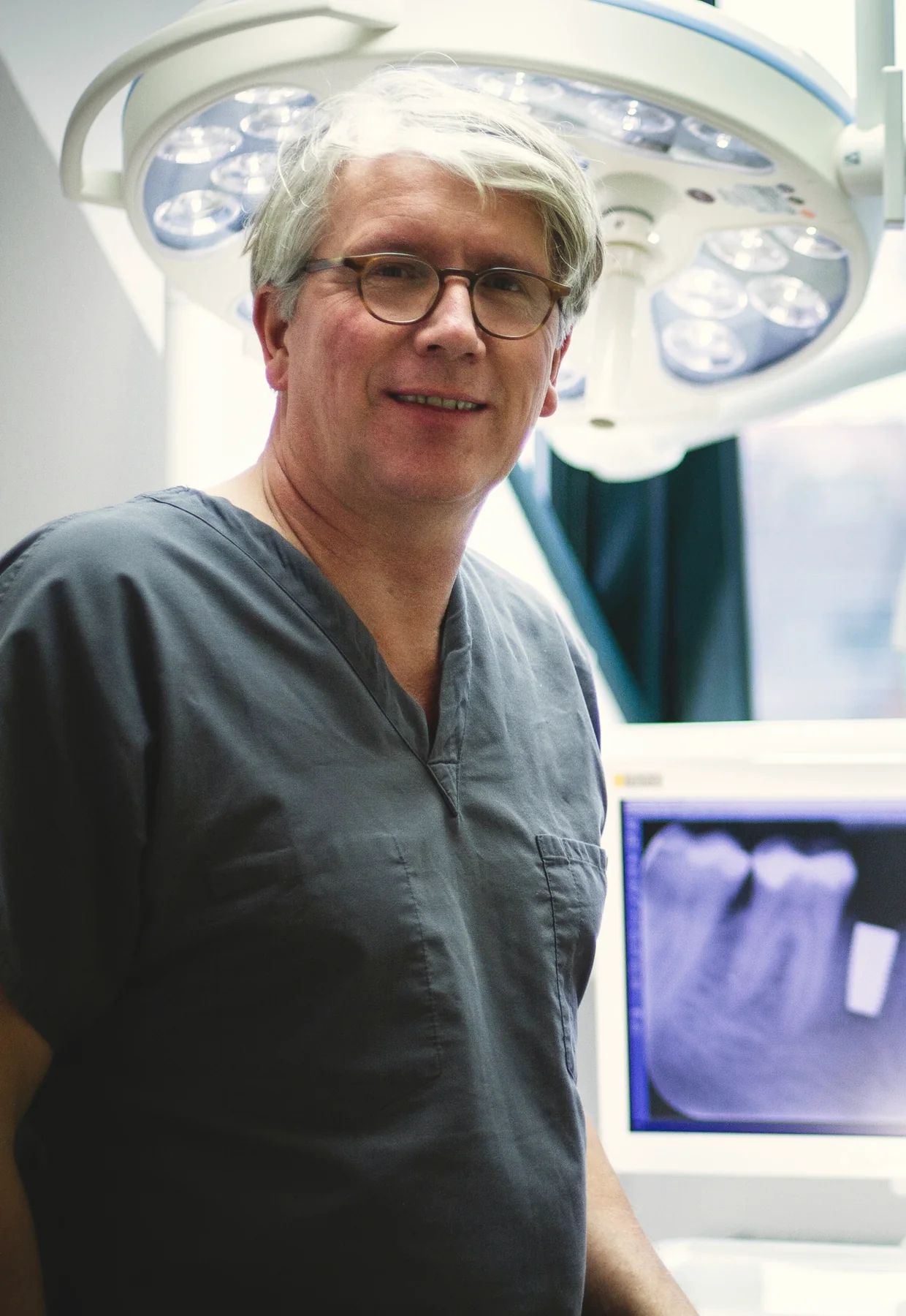Dr. Ralf Lüttmann im Behandlungsraum, im Hintergrund ein Röntgenbild mit Keramikimplantat