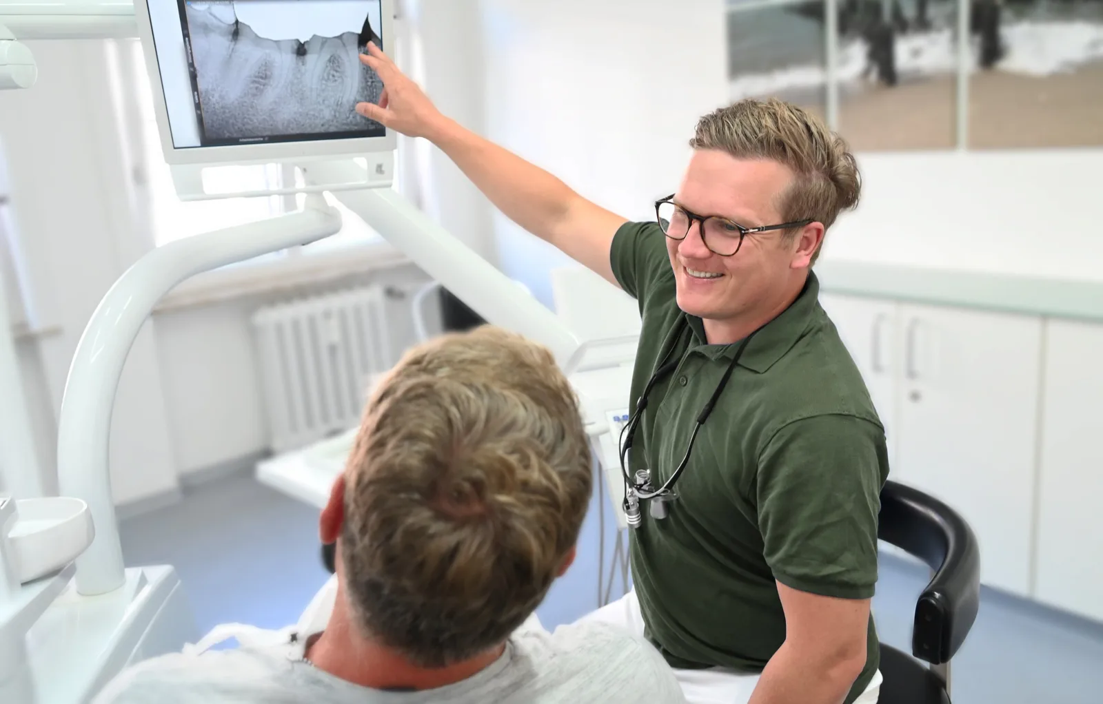 Jan-Ole Lüttmann erklärt einem Patienten am Behandlungsstuhl das Röntgenbild