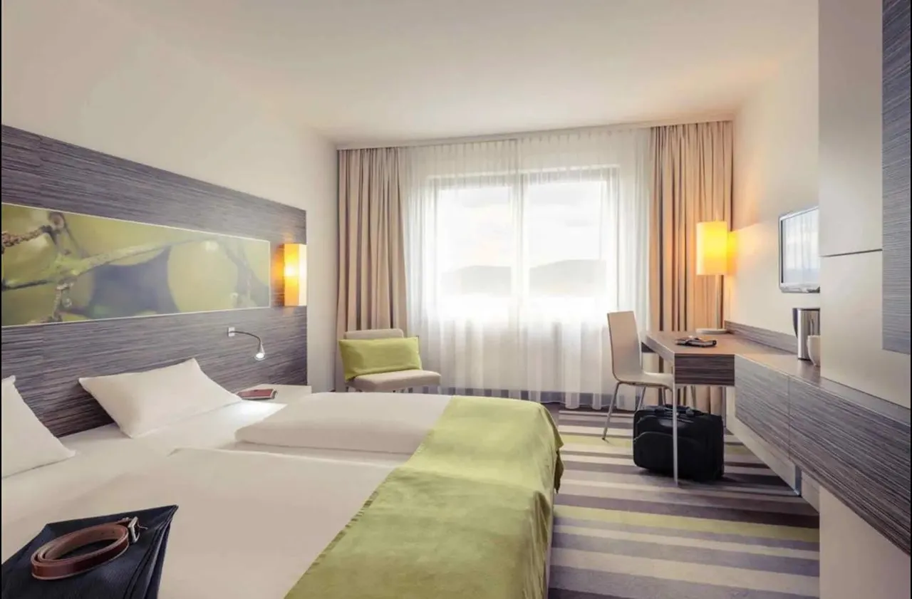 Hell eingerichtetes Hotelzimmer im Mercure Koblenz mit zwei Betten, Schreibtisch und Blick zum Fenster