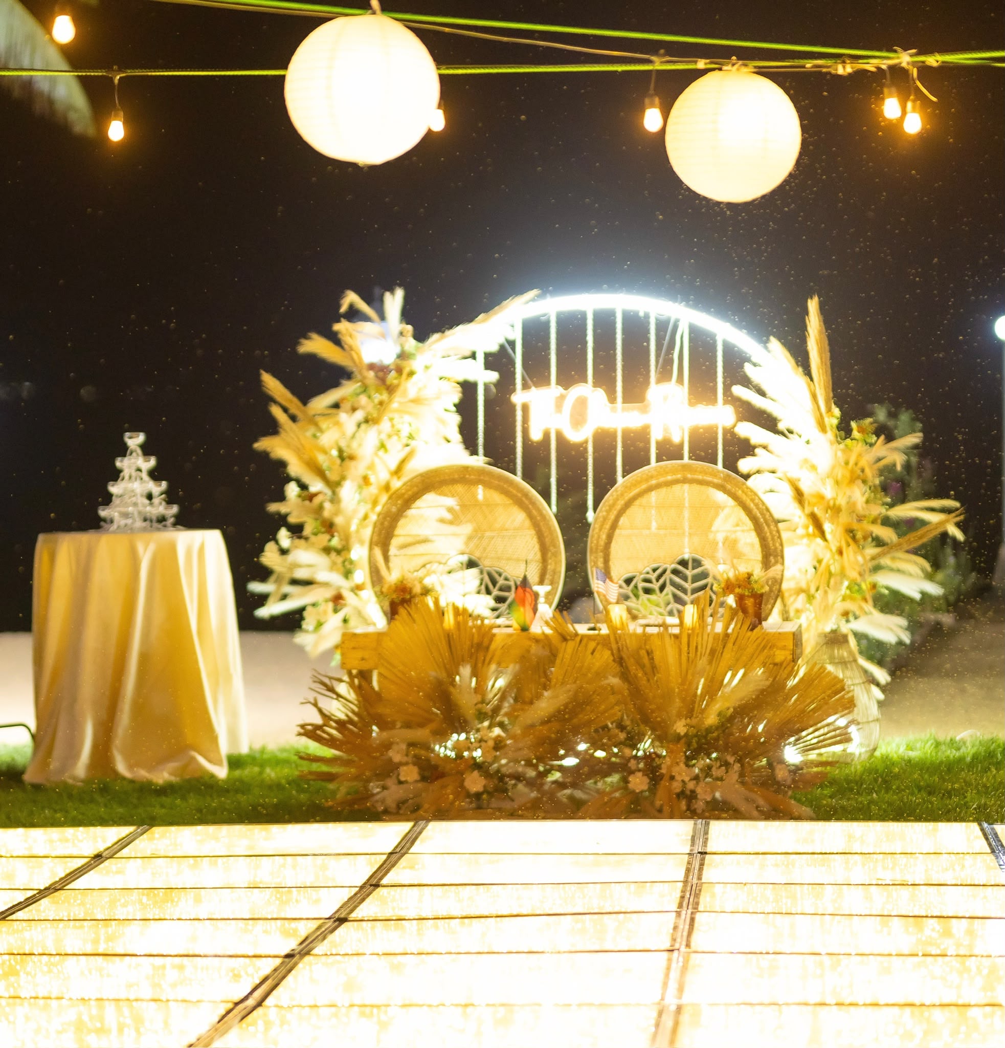 A reception backdrop lit with fairy lights and lanterns on the lawn at night