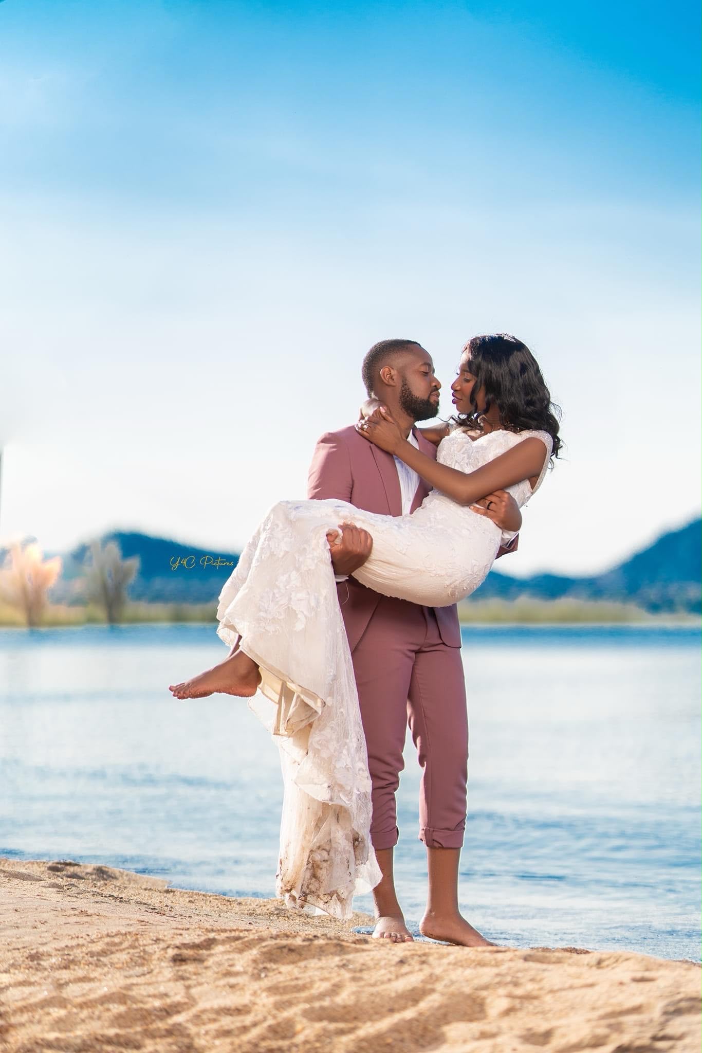A groom carrying his bride along the beach at Senga Bay, Lake Malawi behind them