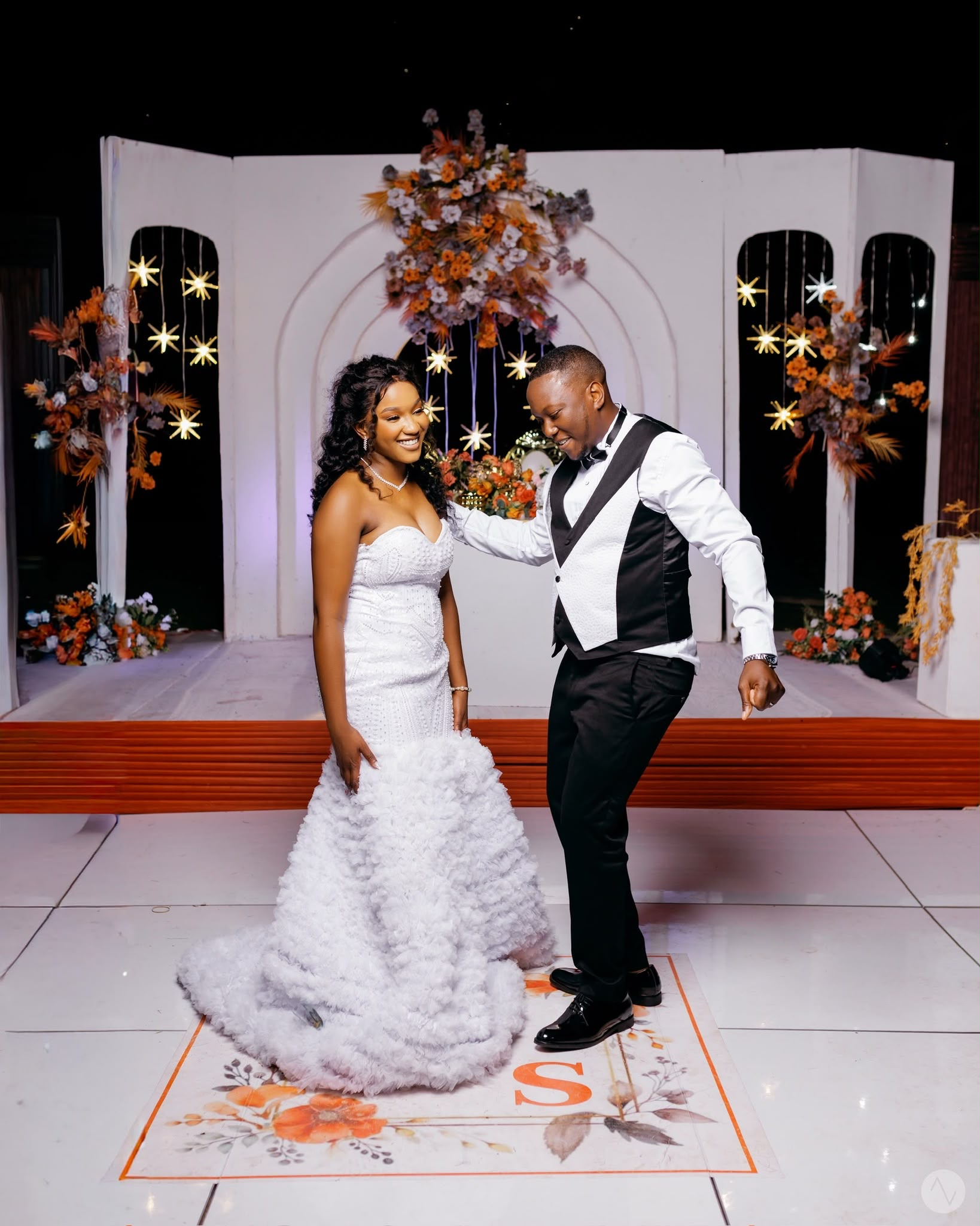 A couple on a white dance floor in front of an orange floral backdrop