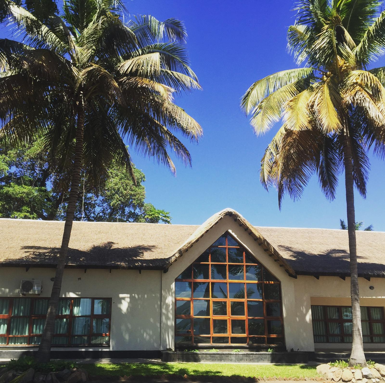 The conference hall at Red Zebra Lodge, a thatched lakeside building framed by palm trees