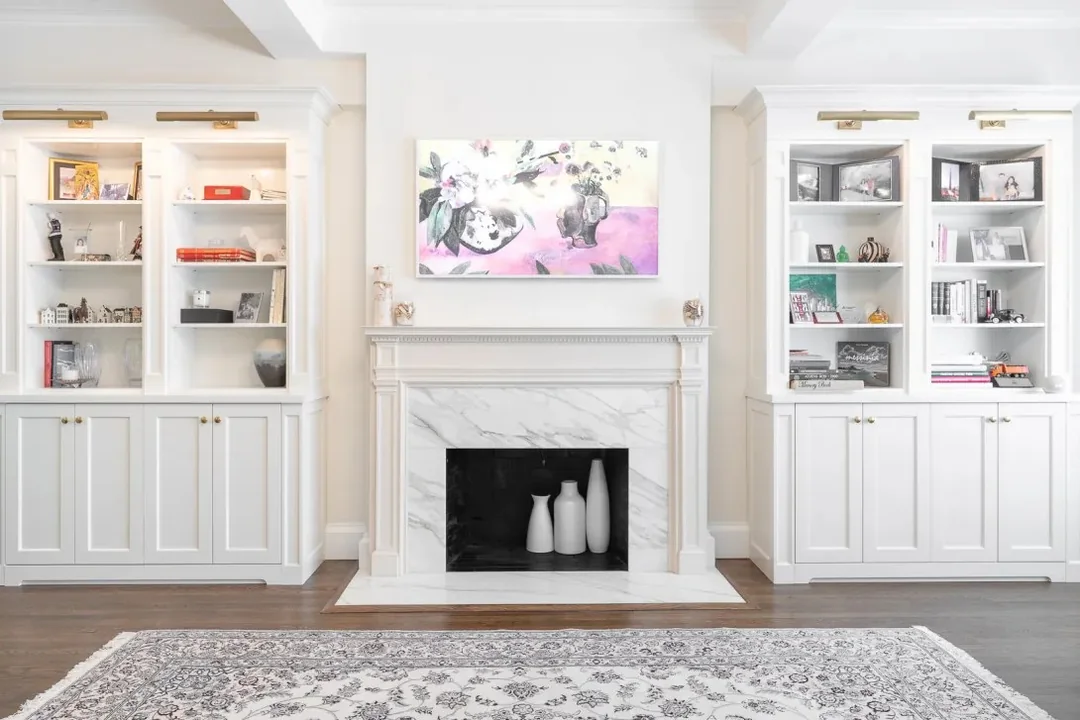 White custom built-in bookshelves and cabinetry flanking a marble fireplace in an elegant living room.