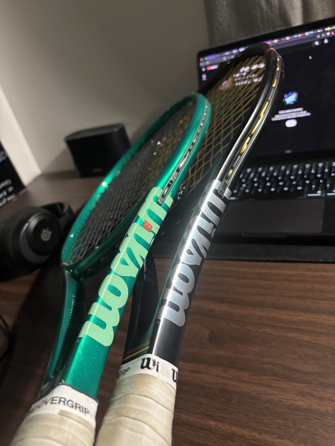 Close-up of the Wilson logos on a green racket and a black racket, white overgrips at the base