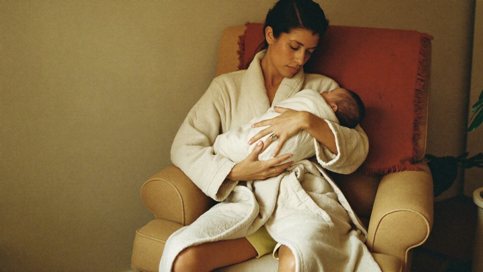 A mother practices holding and feeding her newborn in an armchair