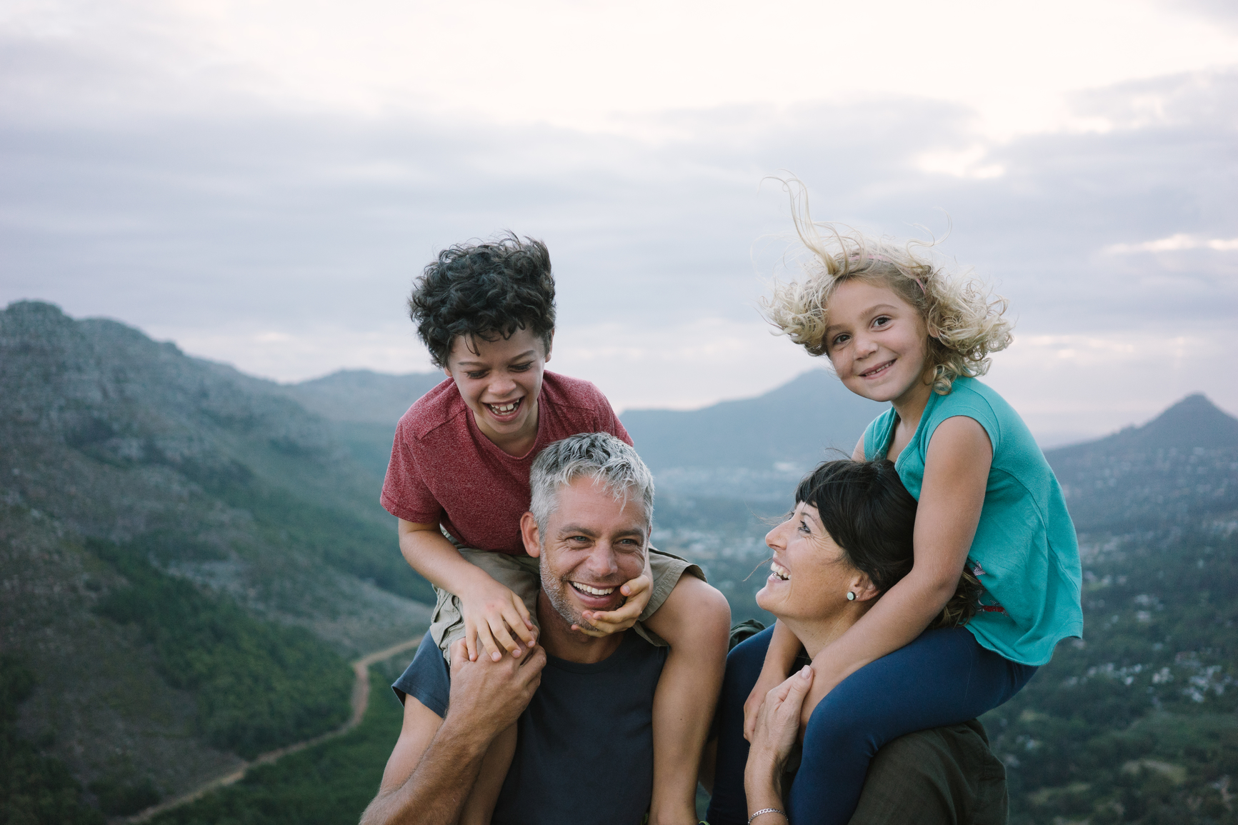 Family laughing together on a hillside, children on their parents' shoulders