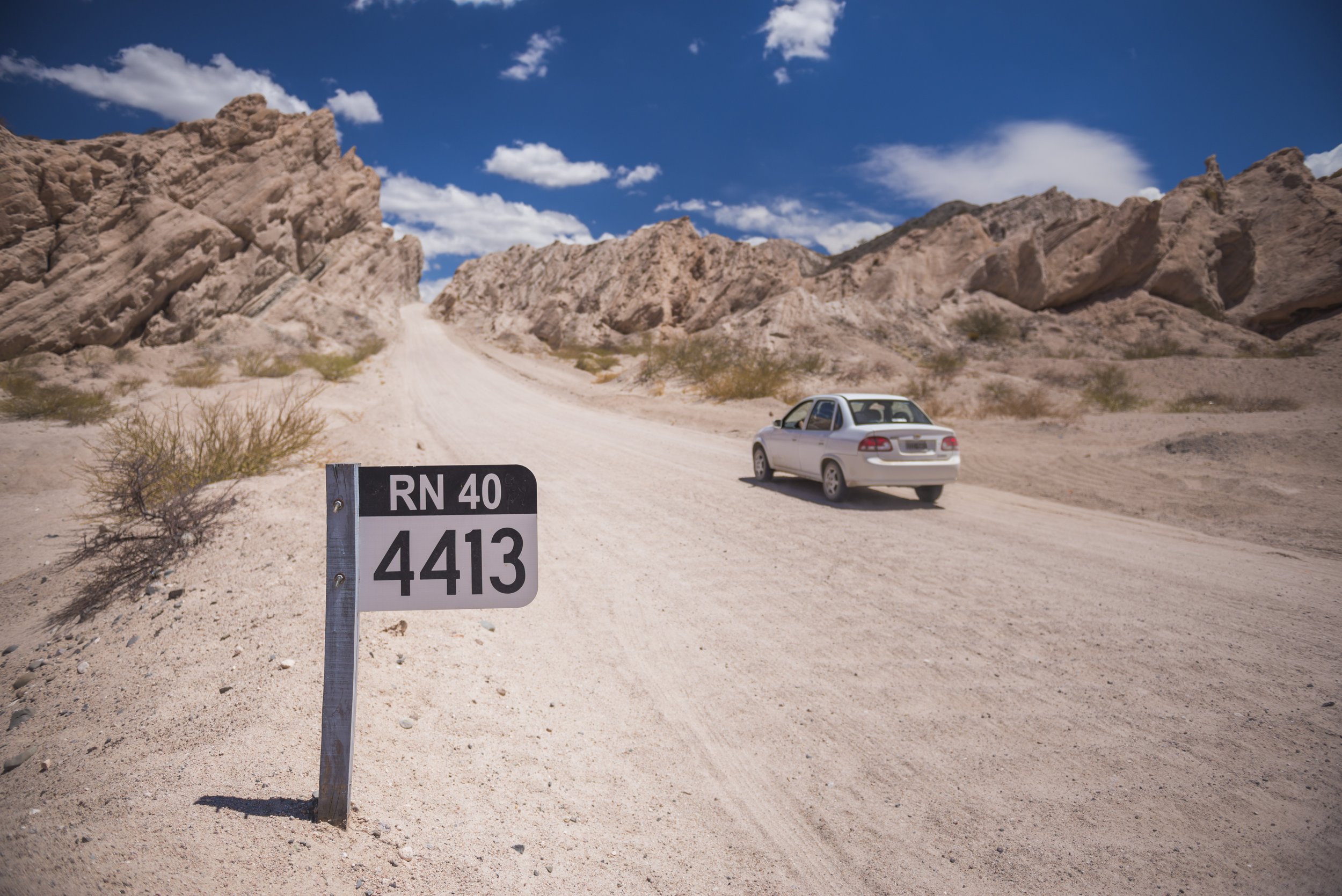 Auto blanco circulando por la Ruta Nacional 40 de ripio entre las formaciones de la Quebrada de las Flechas.