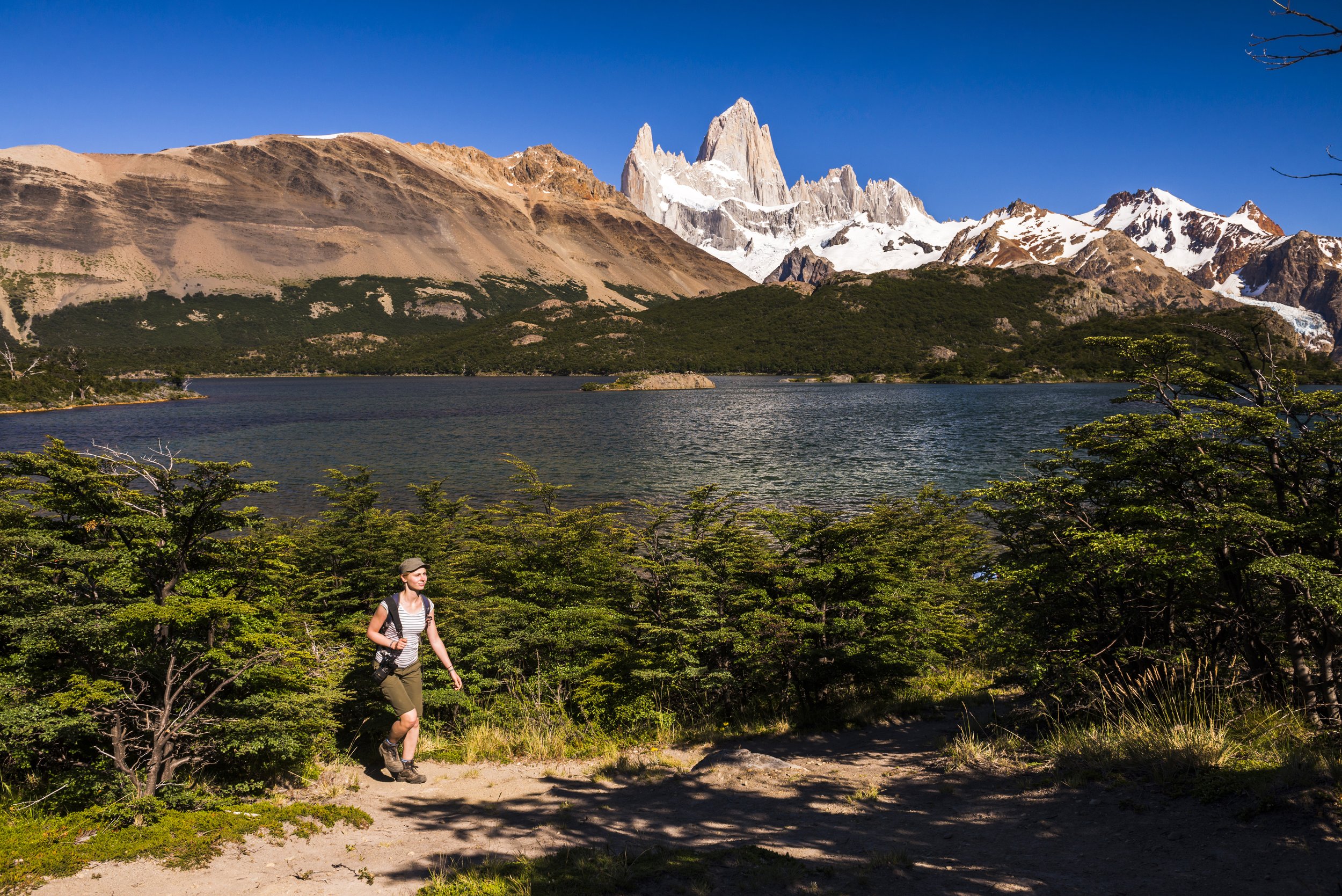 Una mujer camina por un sendero con vista a la Laguna Capri y el Cerro Fitz Roy nevado.