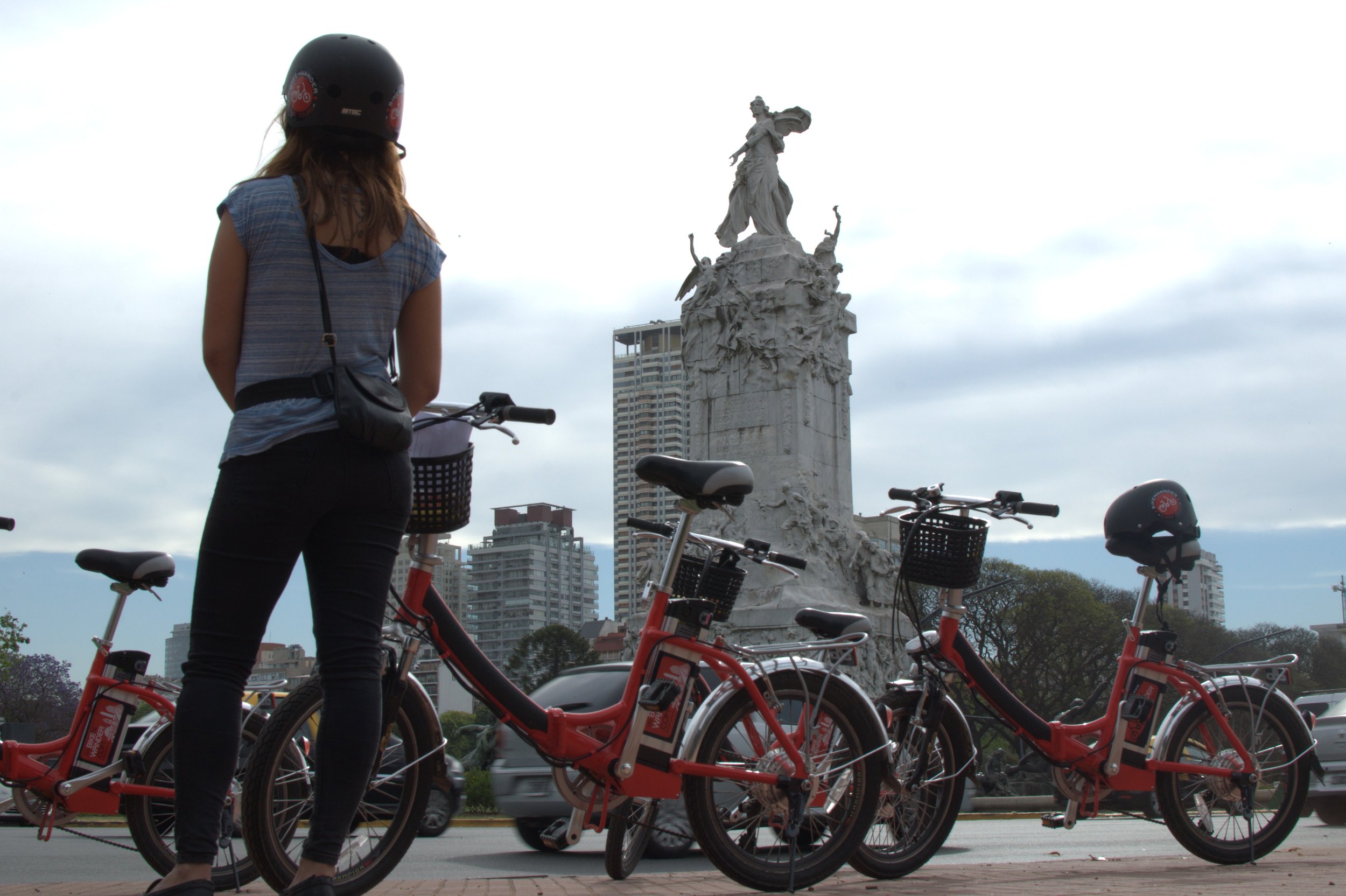 Ciclista de espaldas observando el Monumento de los Españoles junto a varias bicicletas en Buenos Aires.