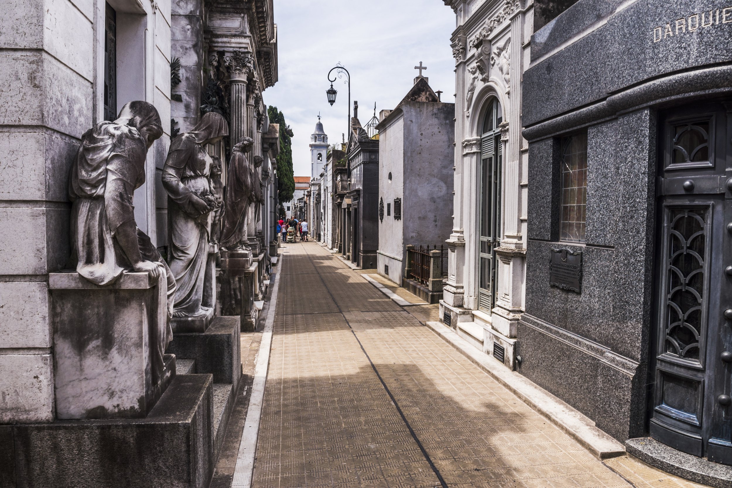 Callejón peatonal flanqueado por mausoleos, estatuas y bóvedas históricas en el Cementerio de la Recoleta.