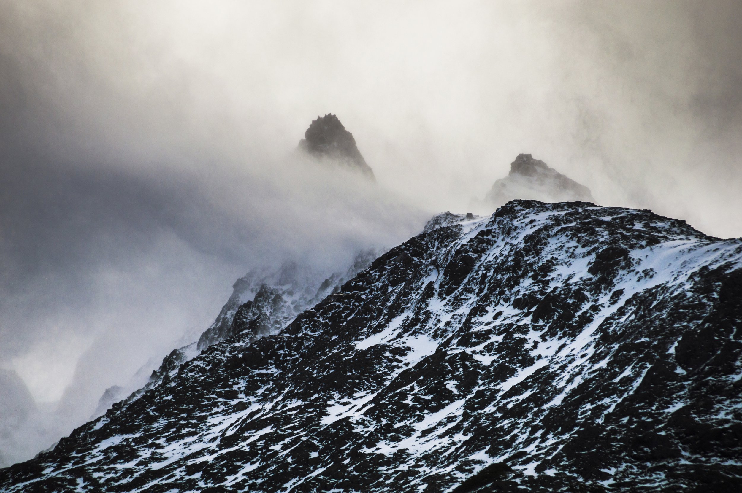 Picos rocosos nevados envueltos en densas nubes y niebla bajo condiciones climáticas adversas en la cordillera.