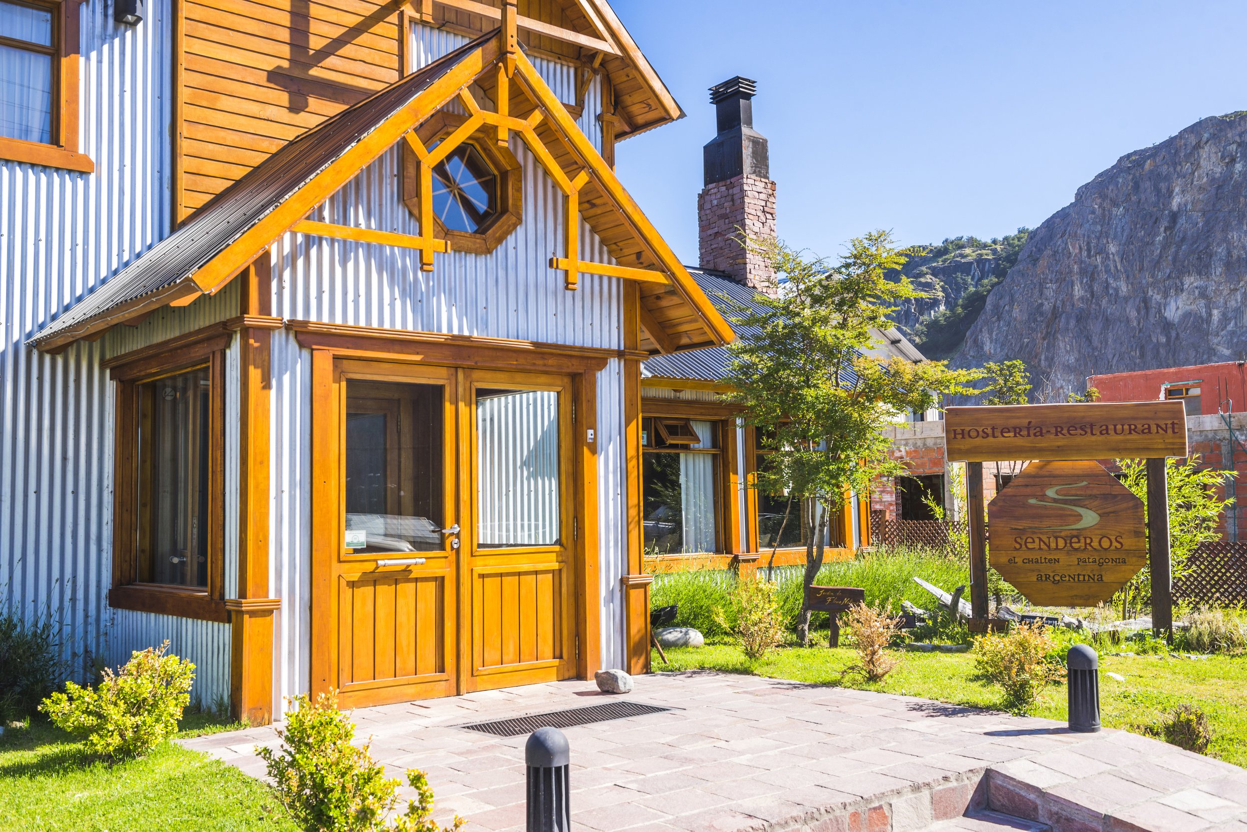 Entrada principal de la hostería Senderos construida en madera y chapa con jardín exterior en El Chaltén.